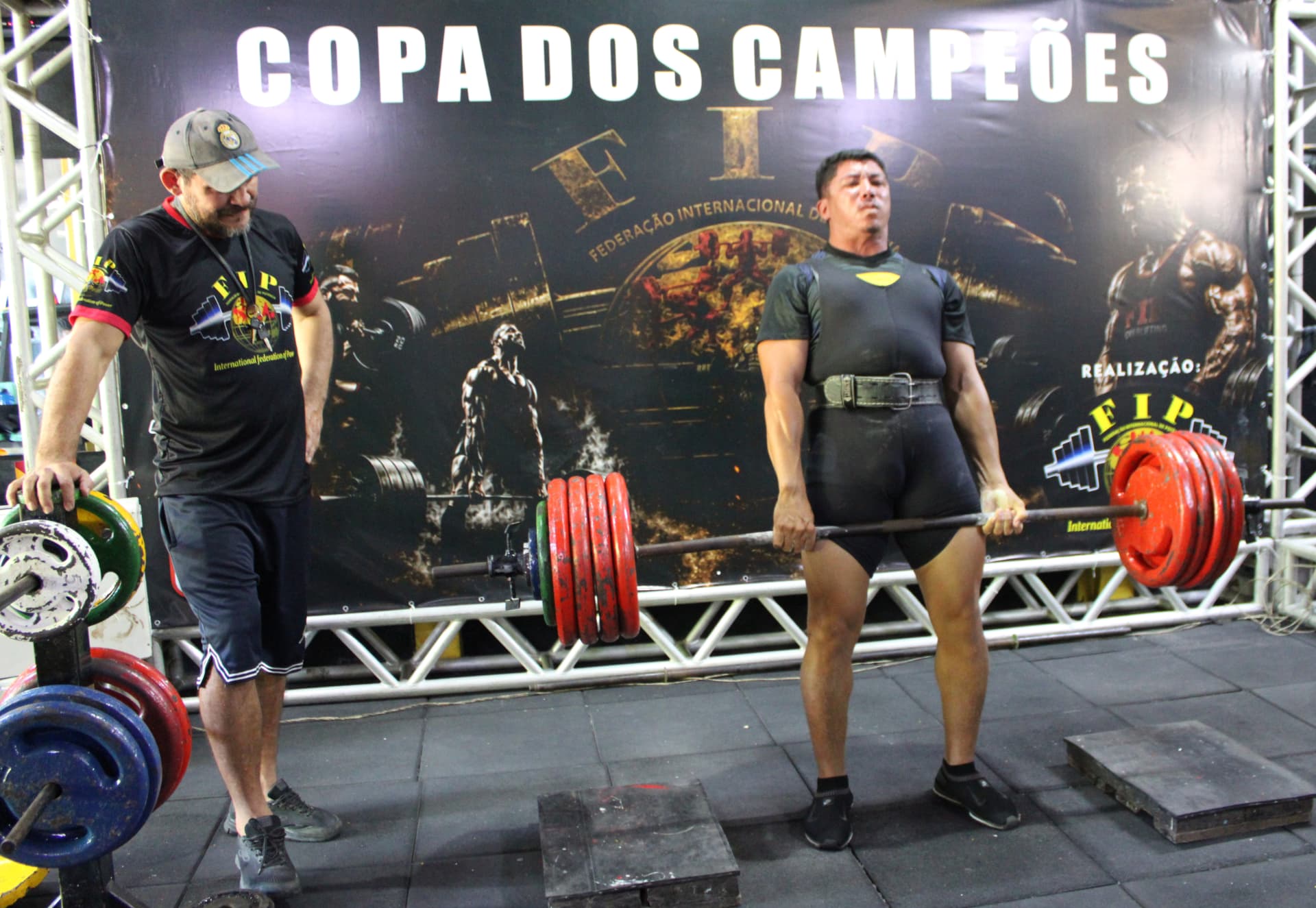 Atleta de macacão executando levantamento terra diante do painel da FIP